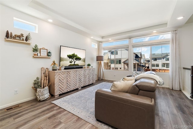 living area with baseboards, wood finished floors, visible vents, and a healthy amount of sunlight
