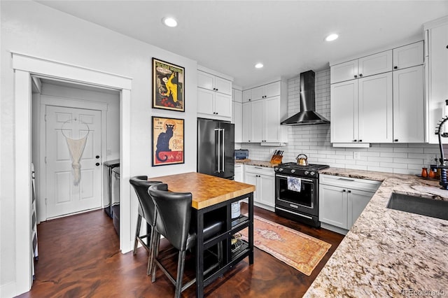 kitchen with wall chimney range hood, high end fridge, light stone countertops, and black range with gas stovetop