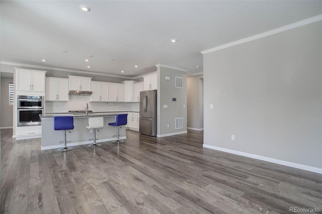 kitchen with appliances with stainless steel finishes, white cabinetry, a breakfast bar area, a center island with sink, and light hardwood / wood-style flooring