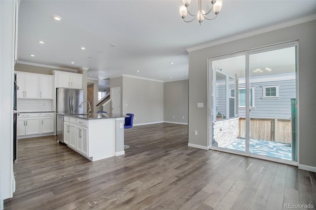 kitchen featuring dark wood-type flooring, white cabinetry, dark stone countertops, an island with sink, and decorative backsplash