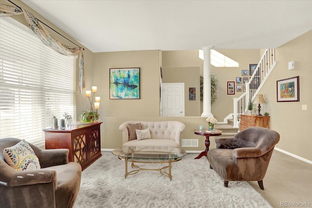 carpeted living area featuring stairway, decorative columns, baseboards, and visible vents