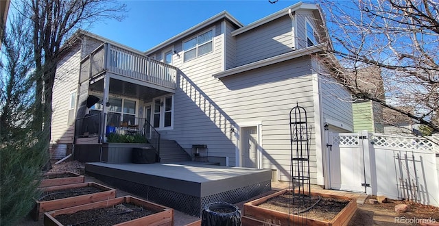 back of house with a balcony, a vegetable garden, a gate, and fence