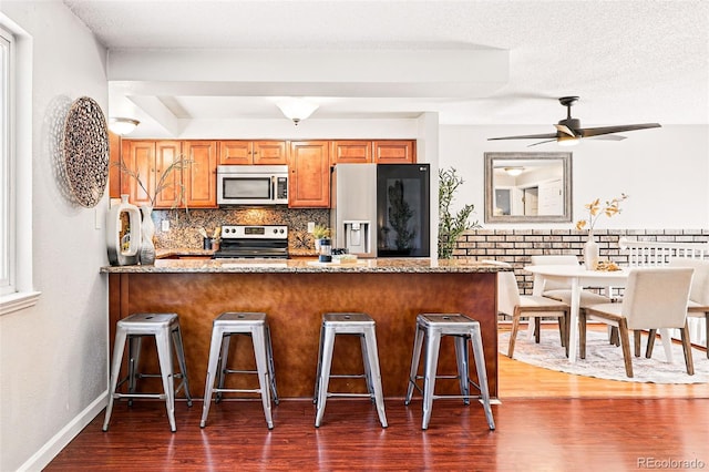 5202 Dillon St, Denver, CO 80239 - kitchen featuring appliances with stainless steel finishes, a peninsula, dark wood-style flooring, a breakfast bar, and tasteful backsplash