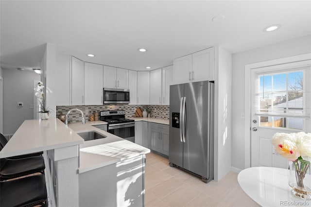 kitchen featuring a kitchen breakfast bar, appliances with stainless steel finishes, kitchen peninsula, sink, and white cabinetry