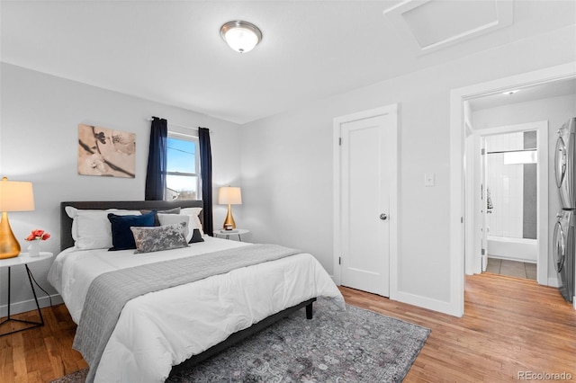 bedroom with connected bathroom, light hardwood / wood-style flooring, and stacked washer / drying machine