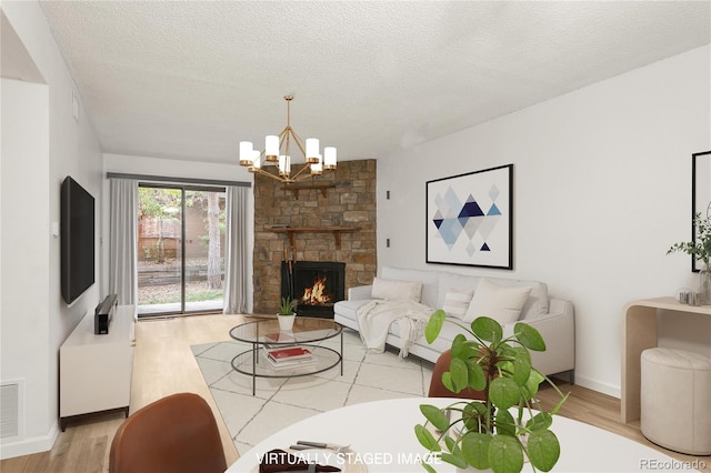 living room featuring a stone fireplace, light hardwood / wood-style flooring, a textured ceiling, and a chandelier