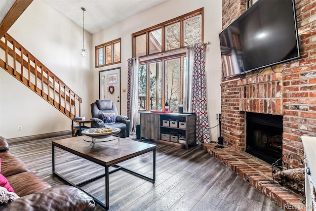 living room with a towering ceiling, wood-type flooring, a brick fireplace, and a textured ceiling