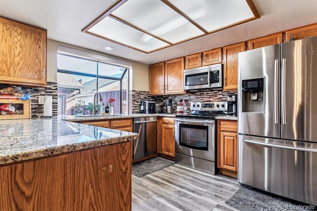 kitchen featuring sink, stainless steel appliances, light stone counters, decorative backsplash, and light wood-type flooring