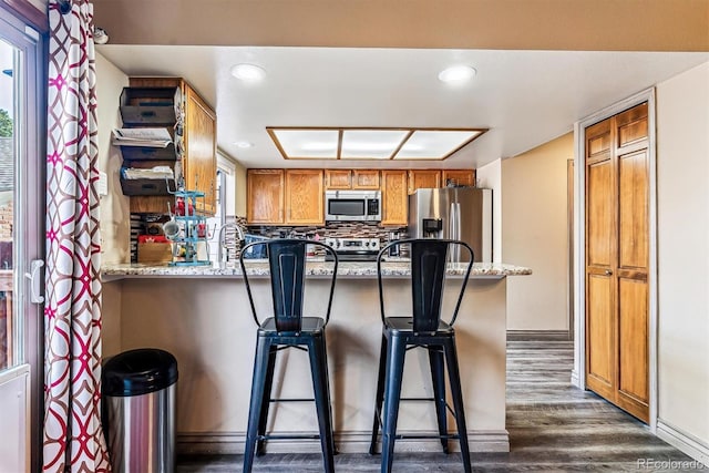 kitchen with a kitchen bar, light stone counters, dark hardwood / wood-style floors, stainless steel appliances, and backsplash