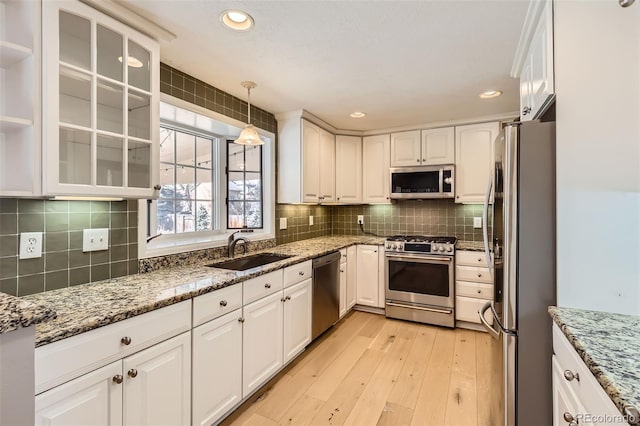 kitchen with light stone counters, glass insert cabinets, white cabinets, stainless steel appliances, and a sink
