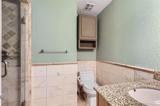 full bathroom with a shower stall, wainscoting, visible vents, and tile walls