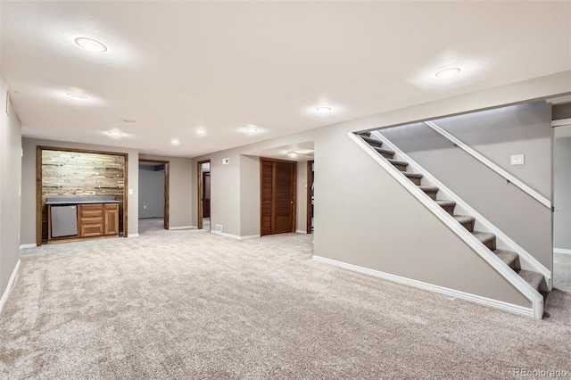 finished below grade area featuring light colored carpet, indoor bar, baseboards, and stairs