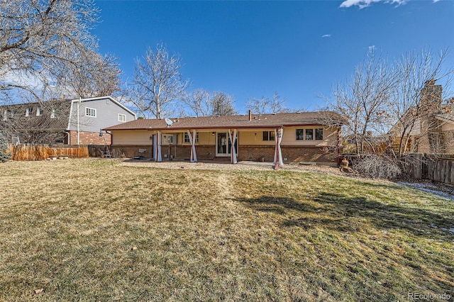rear view of house featuring a yard, brick siding, fence, and a patio