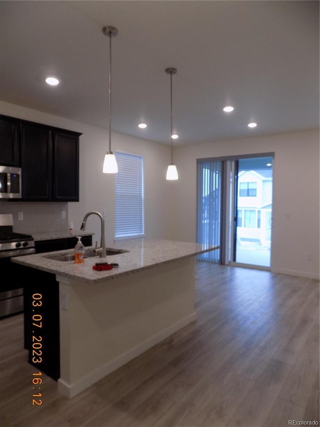 kitchen featuring a sink, light wood-style floors, appliances with stainless steel finishes, decorative backsplash, and light stone countertops