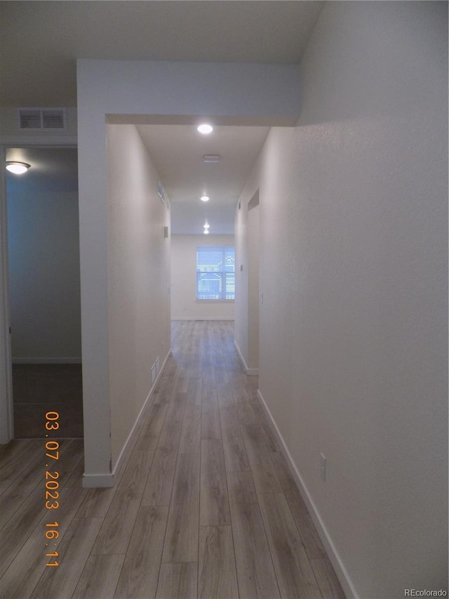 hall with visible vents, baseboards, and wood finished floors