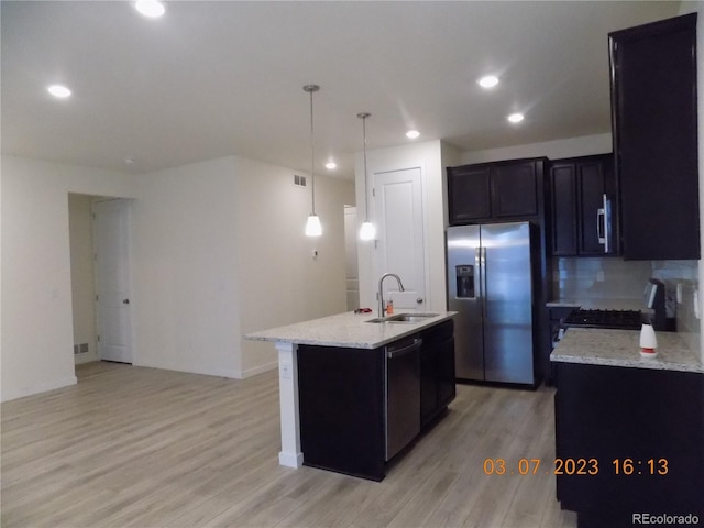 kitchen with light stone counters, appliances with stainless steel finishes, light wood-style floors, and a sink