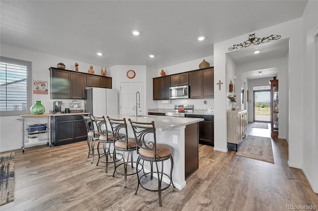 kitchen featuring dark brown cabinets, a breakfast bar, a sink, stainless steel appliances, and light wood-type flooring