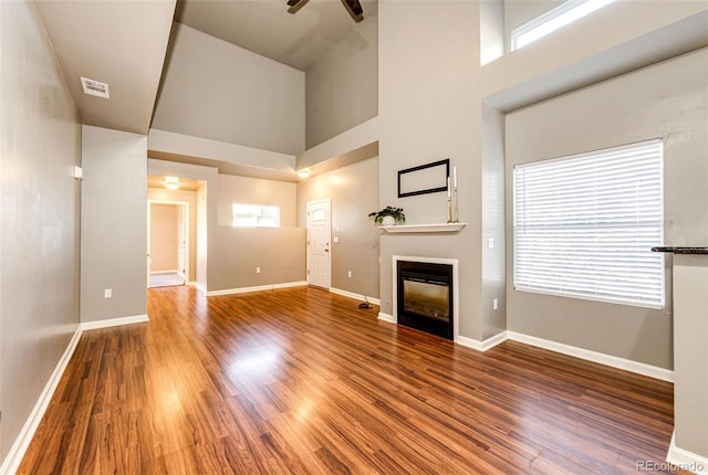 unfurnished living room with ceiling fan, hardwood / wood-style floors, and a towering ceiling