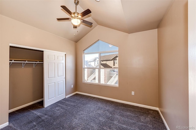 unfurnished bedroom featuring dark colored carpet, a closet, vaulted ceiling, and ceiling fan