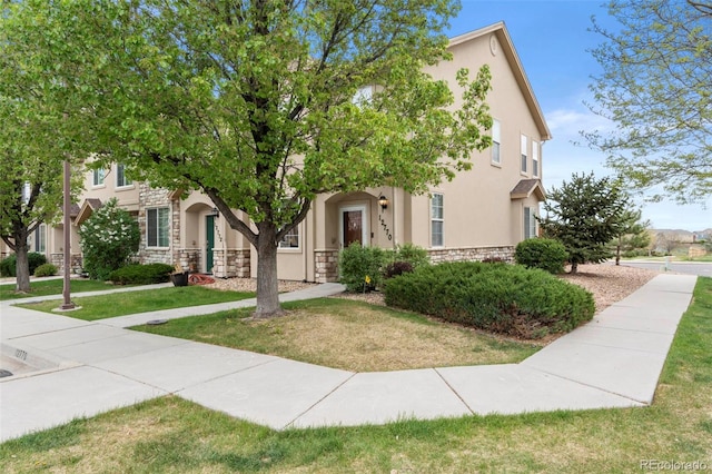 view of property hidden behind natural elements featuring stone siding, stucco siding, and a front yard