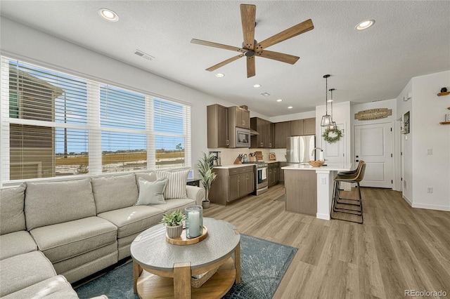 living room featuring ceiling fan, a textured ceiling, and light wood-type flooring