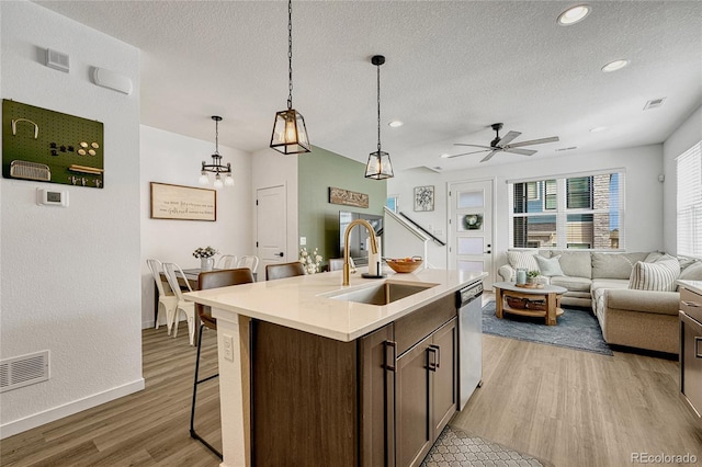 kitchen with pendant lighting, sink, dishwasher, a kitchen breakfast bar, and a center island with sink