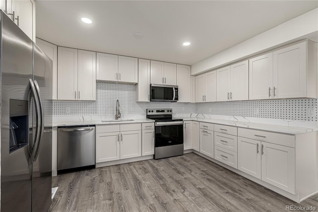 kitchen with sink, white cabinets, light stone counters, stainless steel appliances, and light hardwood / wood-style flooring