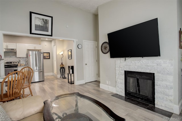 living room featuring a towering ceiling, a fireplace, and light wood-type flooring