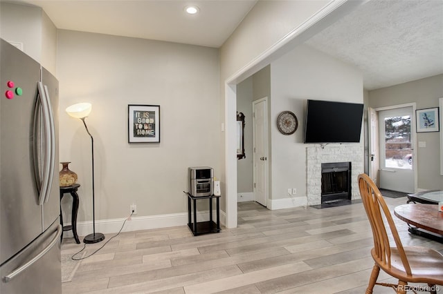 dining room with a stone fireplace, a textured ceiling, and light wood-type flooring