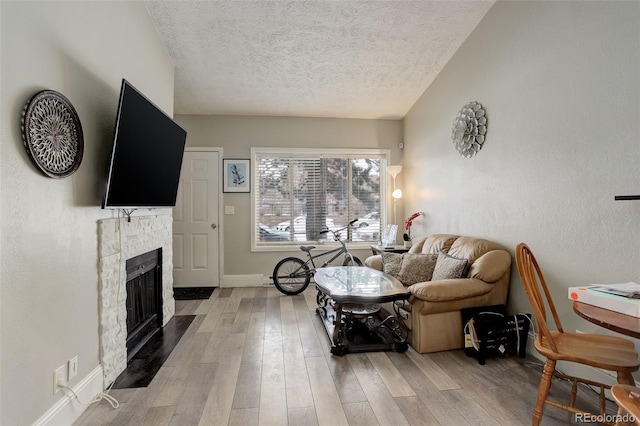 living room featuring a stone fireplace, a textured ceiling, and light wood-type flooring