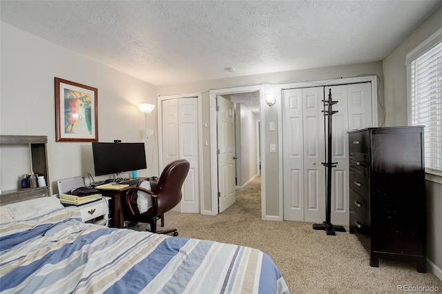 bedroom with light colored carpet, a textured ceiling, and two closets