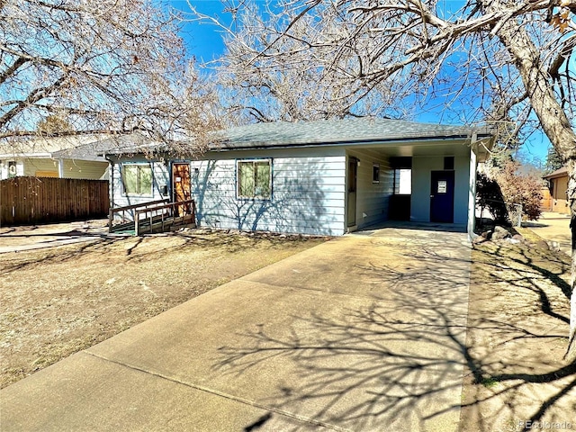 ranch-style home with fence, an attached carport, concrete driveway, and roof with shingles