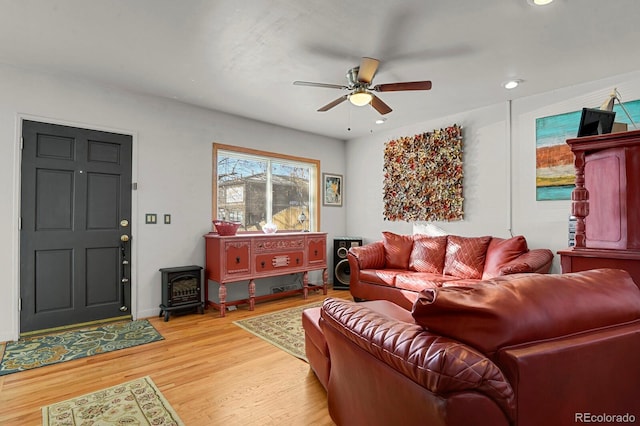 living room featuring a wood stove, light wood finished floors, a ceiling fan, and recessed lighting