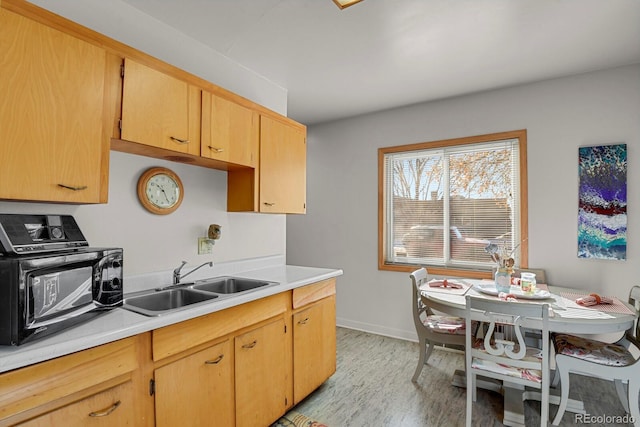 kitchen featuring light countertops, light brown cabinetry, a sink, light wood-type flooring, and baseboards