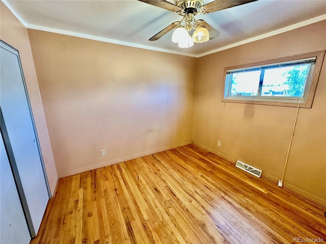 spare room with baseboards, visible vents, a ceiling fan, light wood-style flooring, and ornamental molding