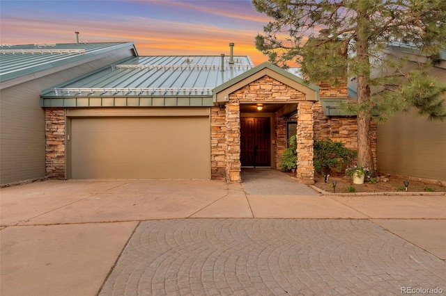 view of front of house featuring stone siding, a standing seam roof, concrete driveway, and metal roof