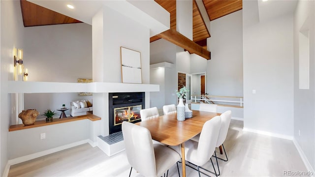 dining area featuring light wood finished floors, baseboards, a glass covered fireplace, recessed lighting, and high vaulted ceiling