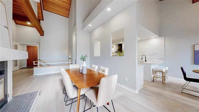 dining room featuring light wood-type flooring, high vaulted ceiling, recessed lighting, baseboards, and beam ceiling