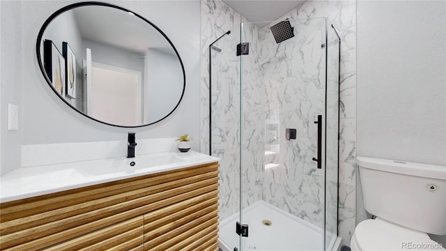 bathroom with toilet, a marble finish shower, and vanity