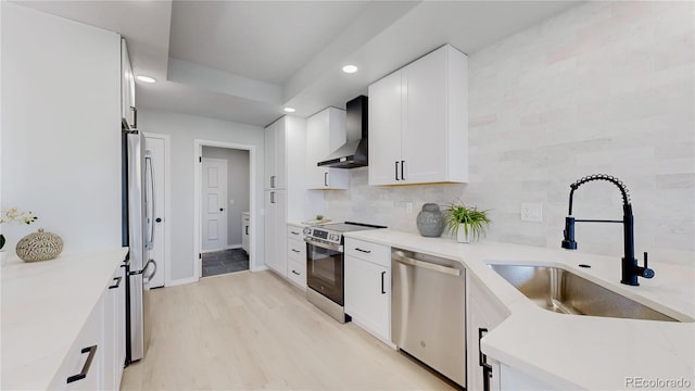 kitchen with wall chimney range hood, appliances with stainless steel finishes, a sink, recessed lighting, and white cabinets
