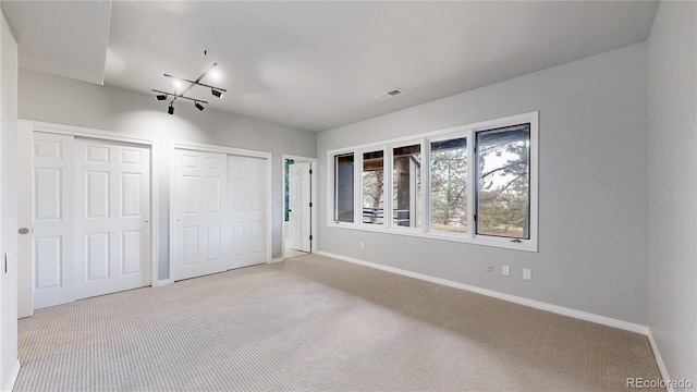 unfurnished bedroom featuring two closets, light carpet, and baseboards