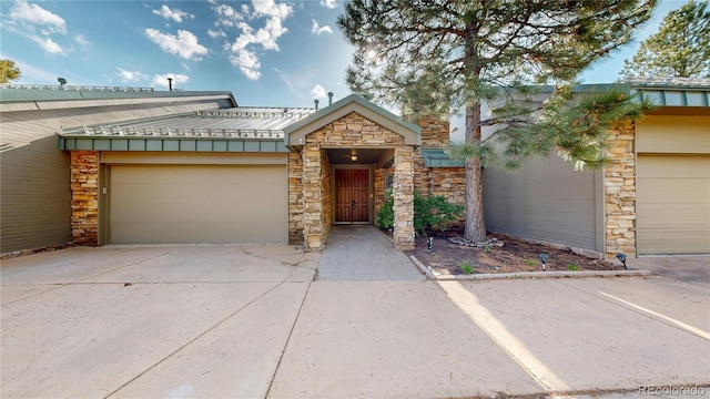 view of front of property featuring stone siding, concrete driveway, metal roof, an attached garage, and a standing seam roof