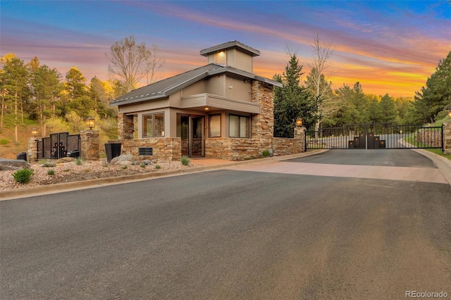 modern home with a gate, stone siding, a standing seam roof, metal roof, and fence