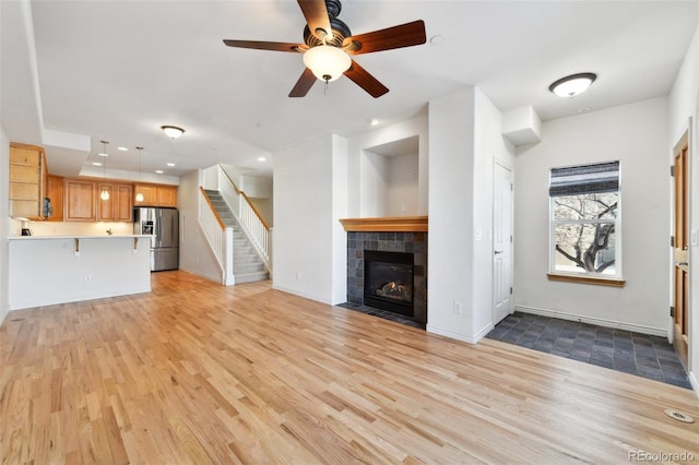 unfurnished living room with light wood-type flooring, ceiling fan, and a tiled fireplace