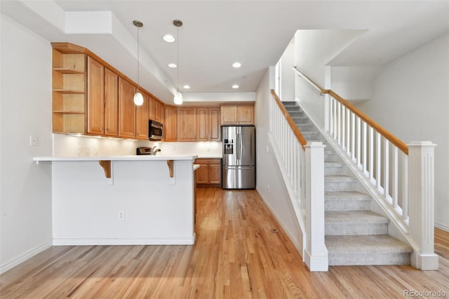 kitchen featuring hanging light fixtures, a breakfast bar area, light wood-type flooring, kitchen peninsula, and stainless steel appliances