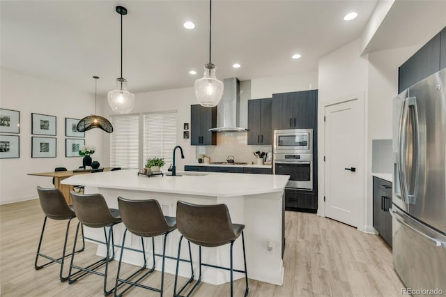 kitchen with a kitchen breakfast bar, light countertops, wall chimney exhaust hood, a sink, and stainless steel appliances