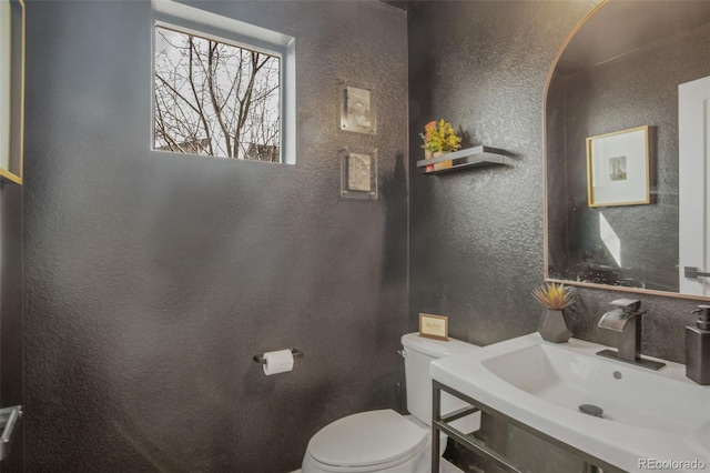 bathroom featuring toilet, a textured wall, and a sink