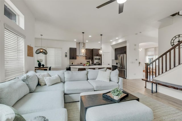 living room featuring stairway, light wood-type flooring, recessed lighting, arched walkways, and a ceiling fan