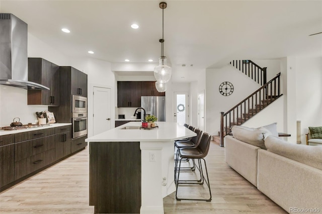 kitchen with wall chimney range hood, a breakfast bar, light wood-style floors, light countertops, and stainless steel appliances