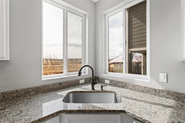 kitchen with white cabinets, a sink, and light stone counters